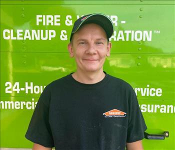 A man standing in front of the rear door of a green truck wearing a SERVPRO labeled shirt and ball cap