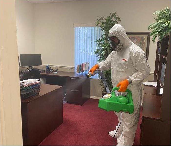 SERVPRO tech, donned in PPE, applying fine disinfectant mist to an office