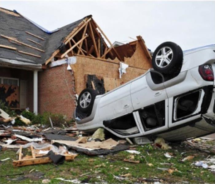 Storm damaged home with upturned car in front yard